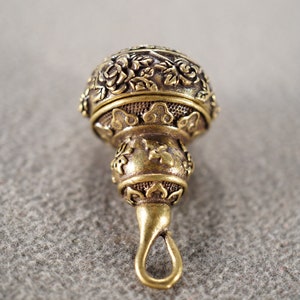 May include: A gold-toned metal pendant with intricate floral and geometric designs. The pendant has a loop at the bottom for attaching to a chain or cord.