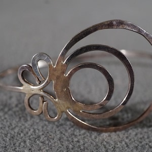 May include: A silver bracelet with a circular design featuring concentric circles and a stylized flower detail.
