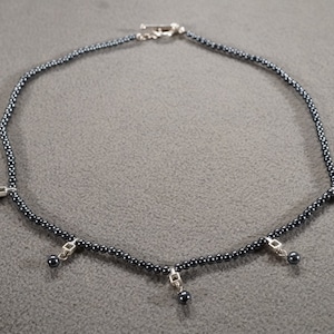 May include: A silver necklace with a black hematite bead chain and five silver charms with black hematite beads hanging from them.