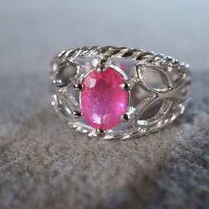 May include: A silver ring with a pink oval gemstone set in a delicate, intricate design.