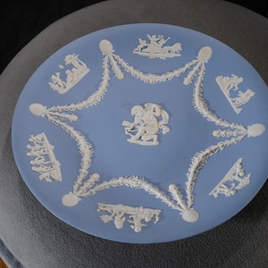 May include: A blue and white ceramic plate with a decorative design of white figures and floral patterns. The plate is a classic example of blue and white transferware.