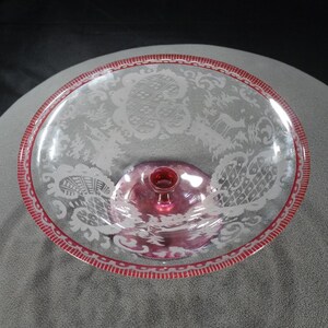 May include: A clear glass pedestal bowl with a red rim and etched floral design. The bowl has a raised centre and a clear glass stem.