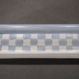 May include: A white ceramic tile trim with a blue and white checkered pattern. The trim has a wavy edge and a blue band around the top.