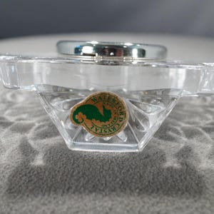May include: A clear glass clock base with a silver clock face and a green and white sticker that reads "WATERFORD CRYSTAL".