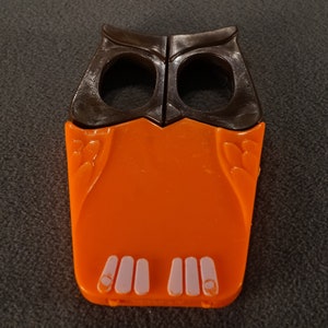May include: Orange and brown plastic owl-shaped finger puppet with white feet.