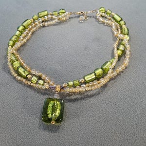 May include: A multi-strand necklace with green and gold beads and a large green pendant.