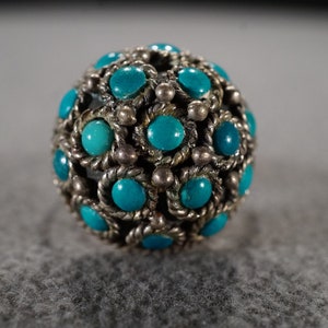May include: A silver ring with a round turquoise stone set in the center. The stone is surrounded by smaller turquoise stones and silver accents.