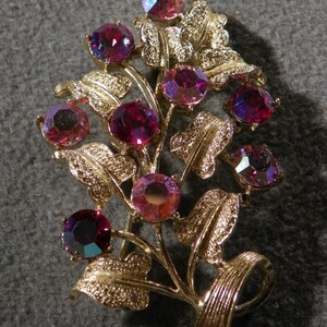 May include: A gold-tone brooch with a cluster of iridescent pink and purple rhinestones set in a leafy design.