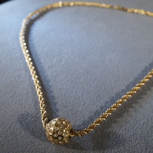 May include: A gold chain necklace with a round pendant covered in small, clear rhinestones.