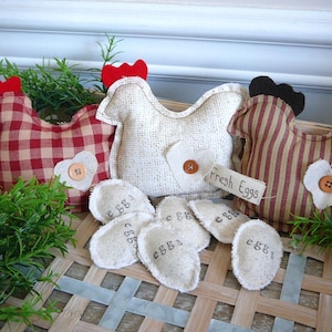 May include: Three fabric chickens, one red and white gingham, one white with brown speckles, and one red and brown striped, with a sign that says "Fresh Eggs".  There are six fabric eggs with the word "eggs" written on them.