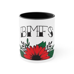 May include: White ceramic mug with a black rim and handle. The mug has a black and white graphic of the letters "BMFS" and a red flower with green leaves.
