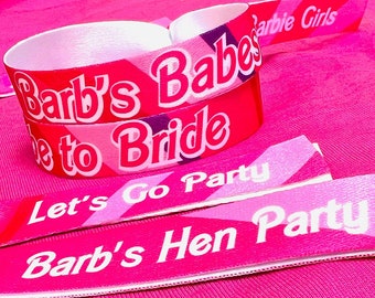 May include: Pink and red wristbands with white text. The wristbands say "Barb's Babes", "Bride to Be", "Let's Go Party", "Barb's Hen Party", and "Barbie Girls". The wristbands are for a bachelorette party.