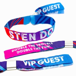 Puede incluir: Varias pulseras de tela coloridas con texto. Una pulsera dice "STEN DO" en letras blancas sobre un fondo morado con detalles rojos. Otra dice "DOUBLE THE TROUBLE DOUBLE THE FUN!" en rosa y blanco. Una tercera dice "VIP GUEST" en blanco sobre azul.