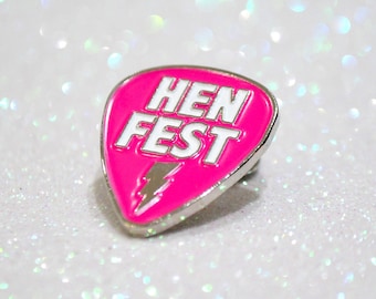 May include: A pink guitar pick shaped enamel pin with a white lightning bolt and the text "HEN FEST" in white.