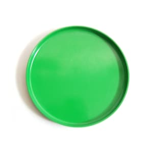 以下が含まれることがあります： 鮮やかな緑色の丸いサービングトレイ。トレイは滑らかで光沢のある仕上がりで、わずかに盛り上がった縁があります。無地の緑色は、白い背景との鮮やかなコントラストを生み出しています。食べ物の提供や装飾品の展示に適しています。