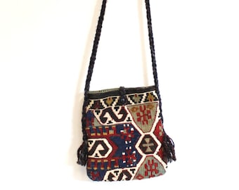 Può includere: Una piccola borsa a tracolla colorata e con motivi, con una tracolla intrecciata nera e nappe. La borsa è realizzata in tessuto intrecciato con motivi geometrici in tonalità di rosso, blu, verde e bianco.