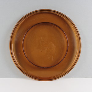 Puede incluir: Un plato de vidrio marrón con un borde elevado y un plato más pequeño en el interior. El plato es perfecto para servir aperitivos o entremeses.