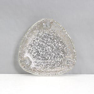 May include: A clear, triangular ashtray with a textured surface and a pattern of small, gold-colored flecks. The ashtray has three small rests for cigarettes and is made of glass.
