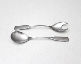 Puede incluir: Un par de utensilios de servicio de acero inoxidable que consta de una cuchara ovalada sólida y una cuchara a juego con un corte en forma de V en el cuenco. Ambos utensilios tienen superficies plateadas pulidas y mangos planos.