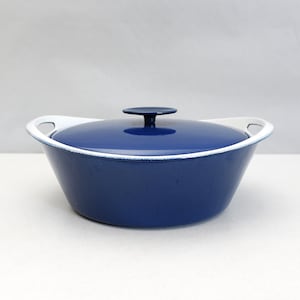May include: A navy blue cast iron Dutch oven with a matching lid. The pot has white handles and a white rim. The lid has a small, round handle. The cookware is designed for cooking and baking.