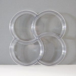 May include: Clear plastic interlocking decorative piece with four circular sections. The sections are connected to each other, forming a clover-like shape. The piece is transparent and sits against a gray background.