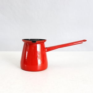 Op de afbeelding: Een kleine, rode emaille koffiepot met een lange handgreep. De pot heeft een zwart interieur en een glanzende afwerking. De handgreep loopt horizontaal vanaf de zijkant. De pot is ontworpen voor gebruik op het fornuis.