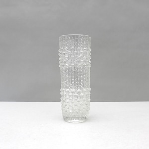 Peut inclure: Un vase cylindrique en verre transparent présentant une surface texturée avec un motif répétitif de bosses arrondies en relief et de lignes verticales. Le verre est transparent et possède une forme uniforme à parois droites.