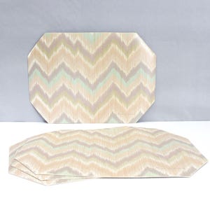 May include: Set of four decorative placemats with a geometric chevron pattern in beige, light green, and gray. The placemats have an octagonal shape and are made of a durable material.