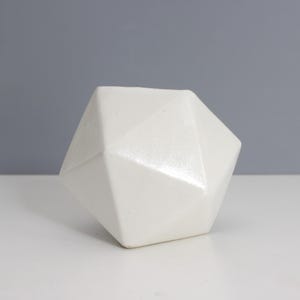 May include: A white ceramic geometric vase with a faceted design. The vase is made of smooth, white ceramic and has a modern, minimalist style.