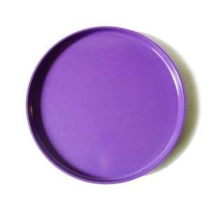 以下が含まれることがあります： 無地の紫色の丸いプラスチックプレート。プレートにはわずかに盛り上がった縁があり、白い背景に配置されています。プレートは鮮やかな紫の色合いです。