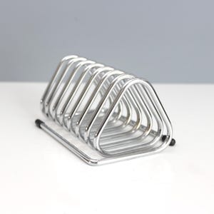 May include: A chrome-finished metal wire rack featuring a series of repeating triangular loops arranged in a row. The structure is supported by a rectangular base frame with small black protective caps on the ends of the wire feet.
