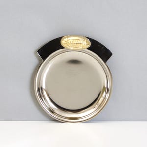 May include: A silver metal tray with a black rim and a gold football design on the top.