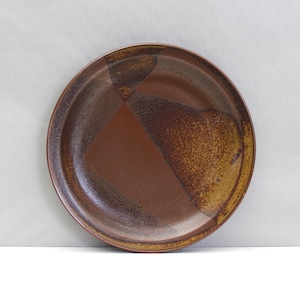 Può includere: Un piatto rotondo in ceramica, marrone e beige. Presenta un design geometrico con una finitura strutturata e macchiettata. Adatto per servire cibo, questo piatto ha un diametro di circa 25 cm.