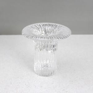 Puede incluir: Un portavelas de vidrio transparente con un borde ancho y texturizado y una base cilíndrica. El vidrio tiene una textura acanalada, creando un juego de luces y sombras. El portavelas está diseñado para sostener una sola vela.