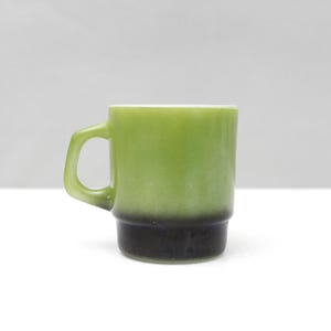 May include: A vintage green and black mug with a handle. The mug has a cylindrical shape with a solid green upper half and a black lower half. The mug is made of glass and is likely from the mid-20th century.