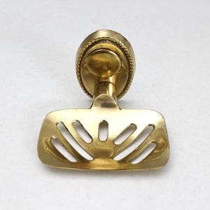 May include: A brass soap dish with a decorative, oval-shaped backplate and a slotted tray. The dish has a shiny, golden finish and is designed for wall mounting. The tray has a series of curved slots for drainage.