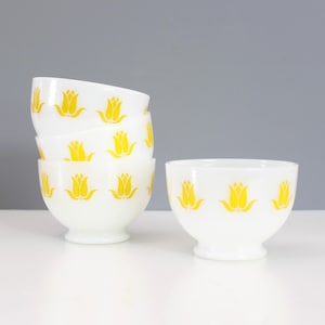 May include: Set of four white milk glass bowls with yellow tulip designs. The bowls are stacked on top of each other.