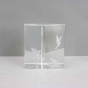May include: A clear, square glass block featuring etched bird designs. The birds are shown in flight and at rest, creating a decorative element. The glass has a ribbed texture on some sides, enhancing the visual appeal.