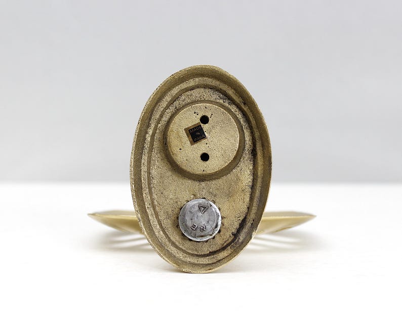 May include: A vintage brass salt shaker with a textured oval base and a small, round top. The shaker has a metallic finish and a small label that reads "MADE IN CHINA".