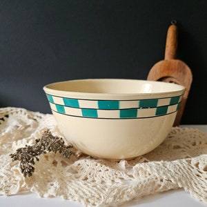 May include: A large, cream-colored mixing bowl with a green and white checkered pattern around the rim. The bowl is sitting on a white crocheted doily.