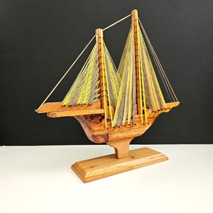 May include: A wooden sailboat with yellow and gray string sails. The sailboat is on a wooden base.