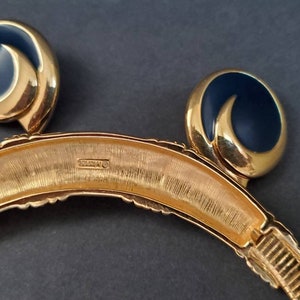 May include: A vintage gold-tone necklace and matching clip-on earrings set. The earrings feature a navy blue enamel swirl design. The necklace has a textured gold finish with a curved shape. The jewelry set is displayed on a dark background.