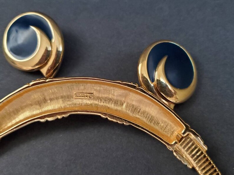 May include: A vintage gold-tone necklace and matching clip-on earrings set. The earrings feature a navy blue enamel swirl design. The necklace has a textured gold finish with a curved shape. The jewelry set is displayed on a dark background.