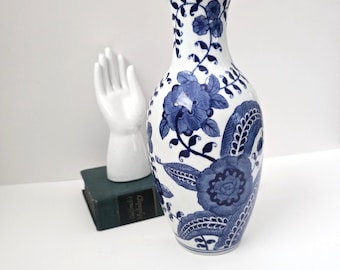 May include: A white ceramic vase with a blue and white floral pattern. The vase has a narrow neck and a wide base.