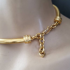 May include: A gold-toned necklace with a textured, ribbed design. The necklace is displayed on a mannequin and features a chain and clasp closure. The jewelry has a bright, shiny finish.