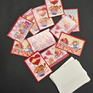 May include: A collection of Valentine's Day cards with red borders and various illustrations. The cards feature images of children, hearts, balloons, and trains. A stack of blank white cards is also present.