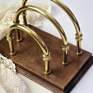 May include: A wooden desk organizer with three arched brass bars. The organizer has a dark brown wooden base and is designed to hold mail or documents. The brass bars are attached to the base with short, decorative posts.