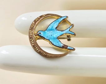 May include: A vintage bird brooch. It features a blue enamel bird in flight, set against a gold-toned crescent moon. The brooch has a pin closure. The bird's wings have brown accents. A decorative accessory.