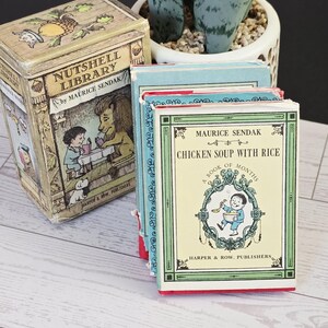 May include: A collection of miniature books, including "Nutshell Library" and "Chicken Soup with Rice" by Maurice Sendak. The books feature colorful illustrations and text, with a vintage aesthetic. The books are in a decorative box.