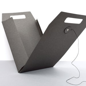 Peut inclure: Une bo&icirc;te en carton noir avec une poign&eacute;e et une fermeture &agrave; cordon. La bo&icirc;te est ouverte et pli&eacute;e en deux.